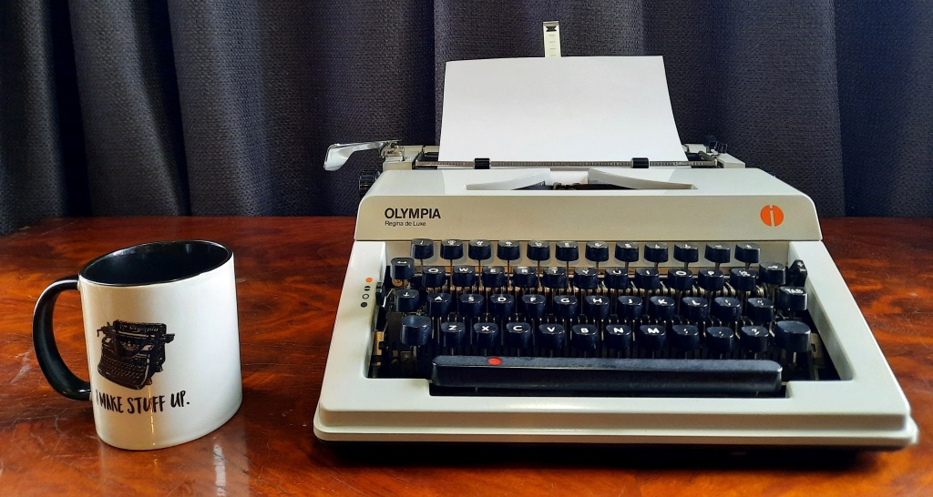 Photo of manual typewriter and mug. Mug has a photo of manual typewriter, and caption "I make stuff up."